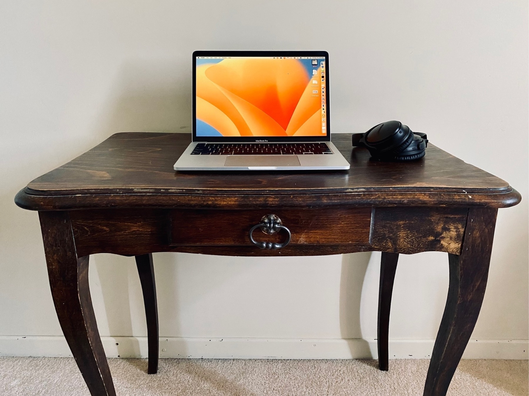 Photo of a small wooden writing desk dominated by a MacBook Pro and over-ear headphones.